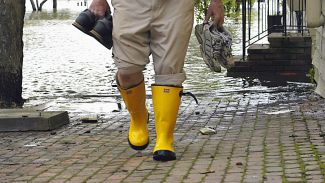 Mann mit Gummistiefel kommt aus seinem überfluteten Keller.